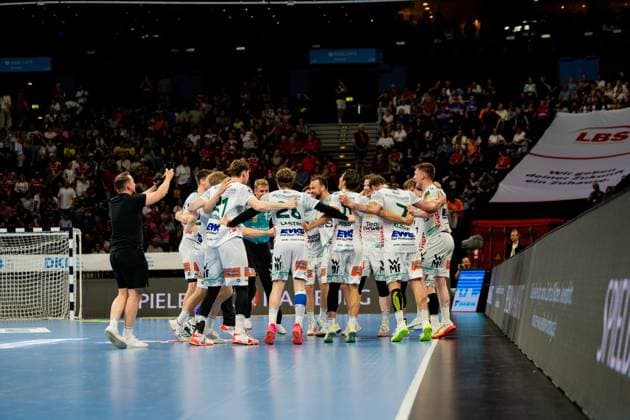 Die Mannschaft von Frisch Auf Göppingen bildet einen Kreis auf dem Spielfeld und feiert einen Erfolg während des Bundesliga-Spiels gegen HSV Hamburg in der Barclays Arena. Die Spieler in weißen Trikots umarmen sich in der Spielfeldmitte, während die Zuschauer im Hintergrund das Geschehen verfolgen. Handball Verein Hamburg vs. Frisch Auf Göppingen Copyright: xPhilippHeistx