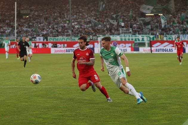 José Enrique Ríos Alonso ( 23; Rot-Weiss Essen) und Branimir Hrgota ( 10; SpVgg Greuther Fürth) kämpfen in einem Laufduell um den Ball. Im Hintergrund ist die vollbesetzte Tribüne des Fürther Stadions mit grün-weißen Fanblöcken zu sehen. José Enrique Ríos Alonso ( 23; Rot-Weiss Essen) im Zweikampf mit Branimir Hrgota ( 10; SpVgg Greuther Fürth)