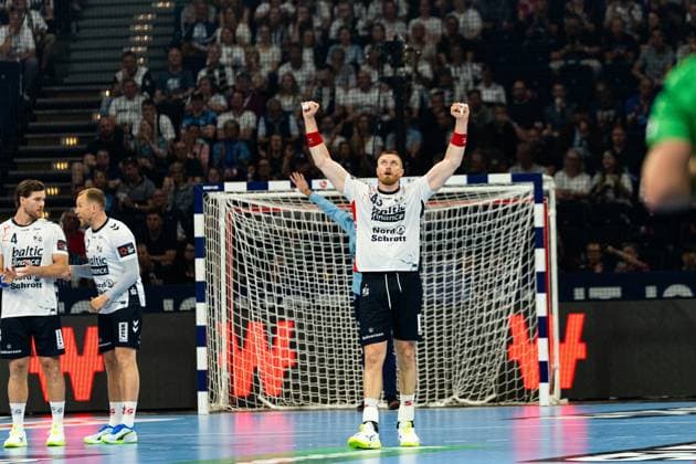 Blaz Blagotinsek ( 43; SG Flensburg Handewitt) reißt beide Arme in die Höhe und jubelt ausgelassen vor dem Tor. Im Hintergrund stehen Johannes Golla ( 3; SG Flensburg Handewitt) und ein weiterer Mitspieler der SG Flensburg Handewitt. MT Melsungen vs SG Flensburg-Handewitt – EHF Finals Hamburg 2026 Copyright: xPhilippHeistx