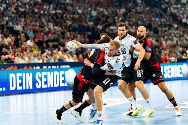 Johannes Golla ( 3; SG Flensburg Handewitt) kämpft sich mit dem Ball durch die Abwehr der MT Melsungen, während Adrian Sipos ( 8; MT Melsungen) im Hintergrund beobachtet. Der Melsunger Verteidiger mit 25 versucht Golla zu stoppen. MT Melsungen vs SG Flensburg-Handewitt – EHF Finals Hamburg 2026 Copyright: xPhilippHeistx