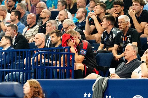 Ein Spieler der MT Melsungen sitzt auf der Auswechselbank und vergräbt sein Gesicht in einem roten Trikot, umgeben von Zuschauern und Teamoffiziellen. Die Körperhaltung drückt Enttäuschung oder Erschöpfung aus. MT Melsungen vs SG Flensburg-Handewitt – EHF Finals Hamburg 2026 Copyright: xPhilippHeistx