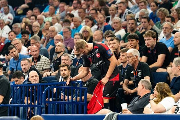 David Mandic (MT Melsungen) an der Seitenlinie beugt sich an der Absperrung zur Tribüne vor und hält ein rotes Handtuch in der Hand. Im Hintergrund verfolgen zahlreiche Zuschauer das Geschehen. MT Melsungen vs SG Flensburg-Handewitt – EHF Finals Hamburg 2026 Copyright: xPhilippHeistx