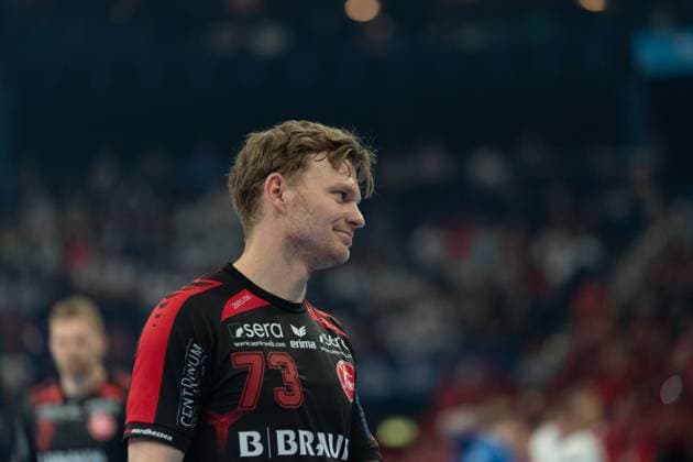 Timo Kastening ( 73; MT Melsungen) steht auf dem Spielfeld und blickt lächelnd zur Seite. Im Hintergrund sind Zuschauer und ein weiterer Spieler von MT Melsungen zu erkennen. MT Melsungen vs SG Flensburg-Handewitt – EHF Finals Hamburg 2026 Copyright: xPhilippHeistx