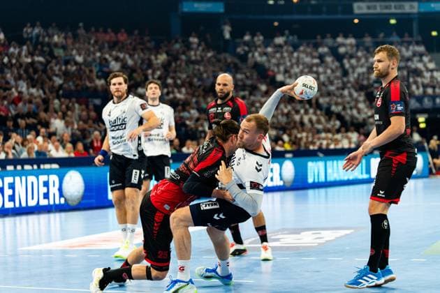 Johannes Golla ( 3; SG Flensburg Handewitt) setzt sich unter Körpereinsatz eines MT-Melsungen-Verteidigers durch und wirft auf das Tor. Im Hintergrund beobachten weitere Spieler beider Teams die Szene vor vollem Zuschauerrang. MT Melsungen vs SG Flensburg-Handewitt – EHF Finals Hamburg 2026 Copyright: xPhilippHeistx