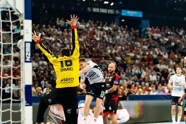 Nebojsa Simic ( 16; MT Melsungen) streckt sich im Tor und versucht einen Wurf eines Flensburger Spielers zu parieren. Adrián Sipos ( 8; MT Melsungen) steht im Hintergrund und beobachtet die Szene. MT Melsungen vs SG Flensburg-Handewitt – EHF Finals Hamburg 2026 Copyright: xPhilippHeistx