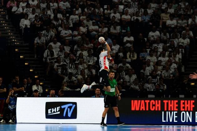 Ein Spieler der SG Flensburg-Handewitt springt hoch und holt zum Wurf aus, während ein Spieler von MT Melsungen im Hintergrund steht. Im Vordergrund ist das EHF TV-Banner sichtbar. MT Melsungen vs SG Flensburg-Handewitt – EHF Finals Hamburg 2026 Copyright: xPhilippHeistx