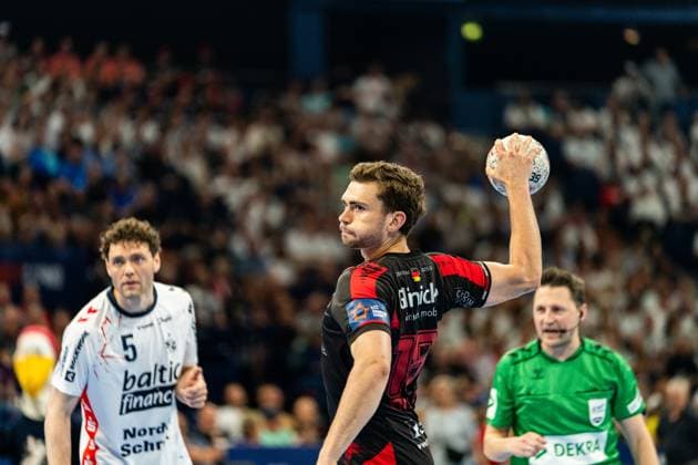 Ein Spieler der MT Melsungen holt zum Wurf aus, während Niclas Kirkeløkke ( 5; SG Flensburg Handewitt) im Hintergrund beobachtet. Ein Schiedsrichter in grünem Trikot verfolgt die Szene. MT Melsungen vs SG Flensburg-Handewitt – EHF Finals Hamburg 2026 Copyright: xPhilippHeistx