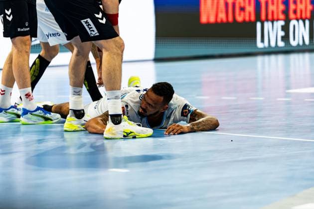 Ein Spieler von Montpellier HB liegt nach einem Zweikampf flach auf dem Hallenboden und blickt auf. Mehrere Spieler der SG Flensburg-Handewitt stehen um ihn herum. Montpellier-Spieler liegt nach Zweikampf auf dem Hallenboden Copyright: xPhilippHeistx