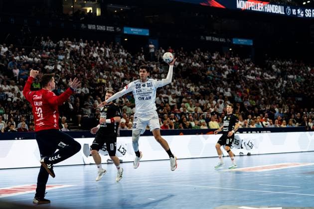 Benjamin Richert ( 22; Montpellier HB) springt hoch und zieht zum Wurf ab, während Spieler der SG Flensburg Handewitt versuchen, den Abschluss zu blocken. Im Hintergrund ist die vollbesetzte Arena mit dem Anzeigetafel-Schriftzug Montpellier Handball vs SG zu sehen. Benjamin Richert ( 22; Montpellier HB) beim Sprungwurf gegen SG Flensburg Handewitt Copyright: xPhilippHeistx