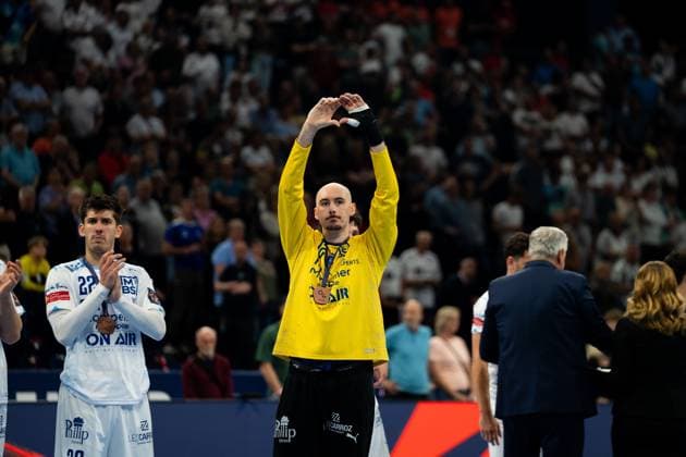 Benjamin Richert ( 22; Montpellier HB) applaudiert bei der Siegerehrung, während ein Teamkollege im gelben Torwarttrikot mit einer Medaille um den Hals die Hände zu einem Herzzeichen über dem Kopf formt. Beide Spieler tragen Bronzemedaillen. Benjamin Richert ( 22; Montpellier HB) bei Siegerehrung mit Medaille Copyright: xPhilippHeistx