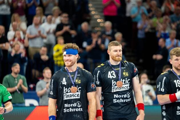 Johannes Golla ( 3; SG Flensburg Handewitt) und Blaž Blagotinöek ( 43; SG Flensburg Handewitt) stehen lächelnd mit Bronzemedaillen um den Hals vor applaudierenden Zuschauern. Beide tragen das schwarze Trikot der SG Flensburg Handewitt. Johannes Golla ( 3; SG Flensburg Handewitt) und Blaž Blagotinöek ( 43; SG Flensburg Handewitt) mit Bronzemedaille Copyright: xPhilippHeistx