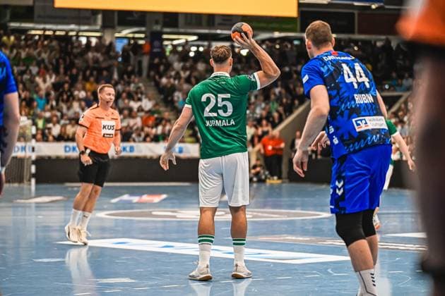Handball, HBL, Frisch Auf! Göppingen - TVB 1898 Stuttgart Spieler 25 Jurmala von Frisch Auf! Göppingen bereitet einen Wurf vor, während ein Abwehrspieler ( 44 Rubin) von TVB Stuttgart Druck ausübt. Im Hintergrund ist ein Schiedsrichter in orangem Trikot zu sehen. Jurmala ( 25; Frisch Auf! Göppingen) beim Wurfansatz gegen TVB Stuttgart