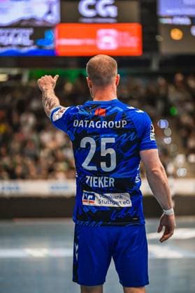 Handball, HBL, Frisch Auf! Göppingen - TVB 1898 Stuttgart Zieker ( 25; TVB Stuttgart) steht mit dem Rücken zur Kamera und zeigt mit dem Finger in Richtung Mitspieler. Im Hintergrund sind die gefüllten Zuschauerrängen und die Anzeigetafel der Halle zu sehen. Zieker ( 25; TVB Stuttgart) gibt Handzeichen auf dem Spielfeld