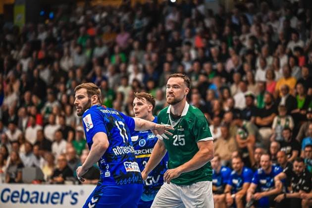 Handball, HBL, Frisch Auf! Göppingen - TVB 1898 Stuttgart #2 Ein Spieler von Frisch Auf! Göppingen ( 25) behauptet sich im Zweikampf gegen einen Spieler des TVB Stuttgart. Im Hintergrund ist eine weitere Person von Frisch Auf! Göppingen zu sehen, während die Halle mit Zuschauern gefüllt ist. Zweikampf zwischen TVB Stuttgart und Frisch Auf! Göppingen ( 25)