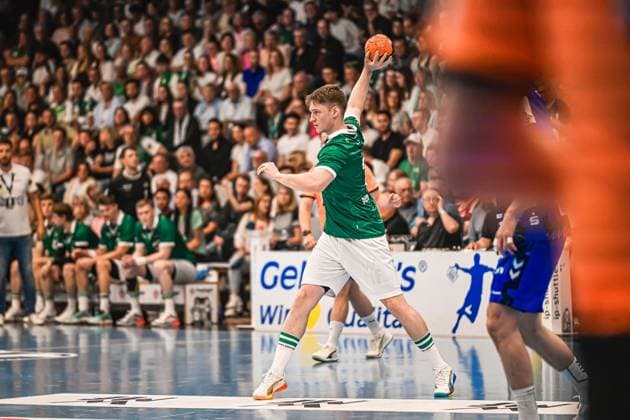Handball, HBL, Frisch Auf! Göppingen - TVB 1898 Stuttgart #2 Ein Spieler von Frisch Auf! Göppingen holt mit dem Ball in der erhobenen Hand zum Wurf aus. Im Hintergrund ist ein Spieler des TVB Stuttgart zu sehen, die Tribünen sind gut gefüllt. Frisch Auf! Göppingen Spieler beim Wurfversuch gegen TVB Stuttgart