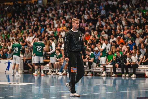 Handball, HBL, Frisch Auf! Göppingen - TVB 1898 Stuttgart #5 Torwart Kristian Sæveras ( 12; Frisch Auf! Göppingen) läuft in schwarzem Torwarttrikot über das Spielfeld und blickt zur Seite. Im Hintergrund sind weitere Spieler von Frisch Auf! Göppingen sowie eine gut gefüllte Zuschauertribüne zu sehen. Kristian Sæveras ( 12; Frisch Auf! Göppingen) läuft über das Spielfeld