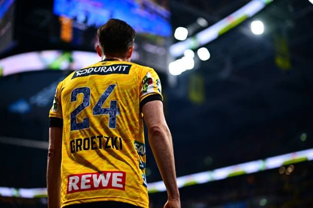 Patrick Groetzki ( 24; Rhein Neckar Löwen) steht mit dem Rücken zur Kamera, sein Trikot mit Nummer und Name ist deutlich zu sehen. Im Hintergrund ist die beleuchtete Halle unscharf erkennbar. Patrick Groetzki ( 24; Rhein Neckar Löwen) von hinten in der Arena Copyright: xMichaelxGelhardtx