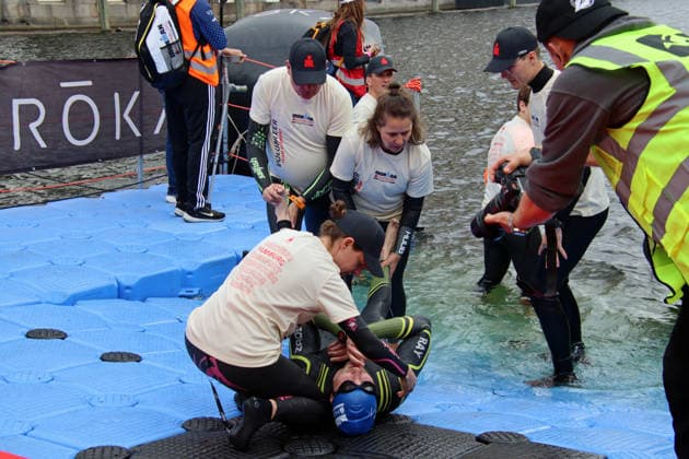 Ironman in Hamburg 2026: Helfer und Helferinnen betreuen einen Athlet, der nach dem Schwimmen Krämpfe in den Beinen bekommen hat.