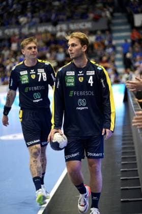 Mathias Rohde Larson ( 4; Rhein Neckar Löwen) betritt mit dem Ball in der Hand die SCHWALBE arena in Gummersbach, gefolgt von Edwin Aspenbäck ( 78; Rhein Neckar Löwen). Im Hintergrund sind die Zuschauertribünen zu sehen. Mathias Rohde Larson ( 4) und Edwin Aspenbäck ( 78; Rhein Neckar Löwen) betreten die Arena