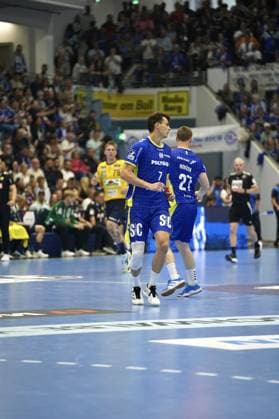 Julian Köster ( 7; VfL Gummersbach) und Kristjan Horžen ( 27; VfL Gummersbach) laufen gemeinsam über das Spielfeld der SCHWALBE arena in Gummersbach. Im Hintergrund ist Edwin Aspenbäck ( 78; Rhein Neckar Löwen) zu sehen. Julian Köster ( 7; VfL Gummersbach) und Kristjan Horžen ( 27; VfL Gummersbach) auf dem Spielfeld