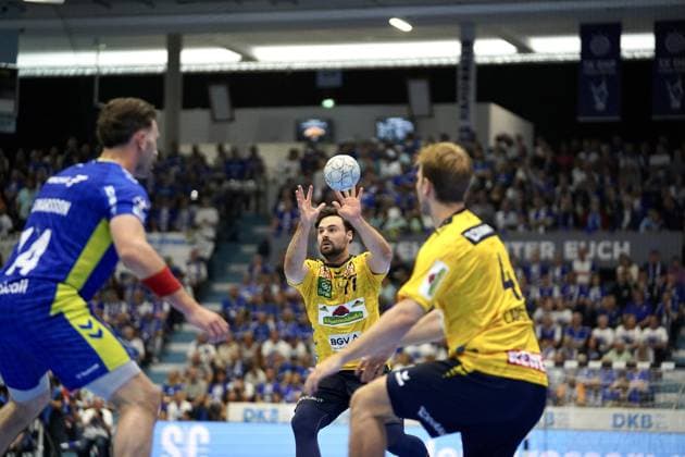 Kentin Mahé ( 22; VfL Gummersbach) nimmt in der SCHWALBE arena einen Wurf vor, während Teitur Einarsson ( 14; VfL Gummersbach) links und ein weiterer Löwen-Spieler rechts im Bild stehen. Die Tribünen sind mit Zuschauern gefüllt. Kentin Mahé ( 22; VfL Gummersbach) beim Wurf gegen Rhein Neckar Löwen