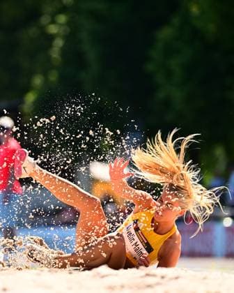 Elvelin Malm aus Schweden landet explosiv in der Sandgrube beim Weitsprung, umgeben von aufspritzenden Sandpartikeln und fliegenden Haaren. Der Name Elvelin Malm ist auf der Startnummer im Bild lesbar. Elvelin Malm (Sweden) beim Weitsprung im Michael-Hoffmann-Stadion Mannheim