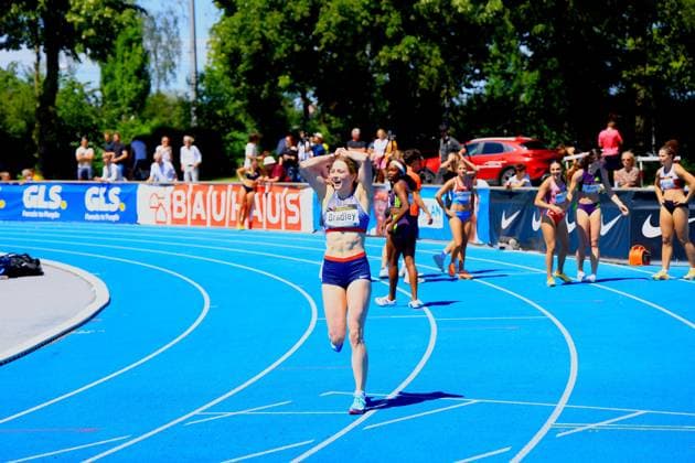 Lily Bradley (Great Britain, 181) reißt jubelnd die Arme hoch nach dem Zieleinlauf auf der blauen Tartanbahn im Michael-Hoffmann-Stadion Mannheim. Im Hintergrund sind weitere Athletinnen sowie Zuschauer und Werbebanden von GLS und Bauhaus zu sehen. Lily Bradley ( 181) jubelt nach dem Zieleinlauf im Michael-Hoffmann-Stadion Mannheim