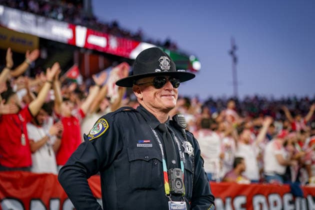 USA: Fußball FIFA World Cup, WM, Weltmeisterschaft, Fussball 2026 Gruppenphase Gruppe J Österreich vs Jordanien San Francisco Bay Area Stadium Levi™s Stadium (Santa Clara County, Kalifornien): Ein Sheriff überwacht das Geschehen am Spielfeldrand, während Fans im Hintergrund jubeln. Sicherheitskräfte während eines FIFA-WM-2026-Spiels, Sheriff, Deputy Sheriff, Law Enforcement, Public Safety, Security, Crowd Management, Polizeipräsenz, Einsatzkräfte, Bodycam, Funkgerät, Uniform, Sonnenbrille, Stadionsicherheit, Event Security, Fan Zone, Zuschauer, Tribüne, Jubel, Fanatmosphäre, Fußballfans, USA, World Cup 2026, Impressionen, Symbolfoto.
