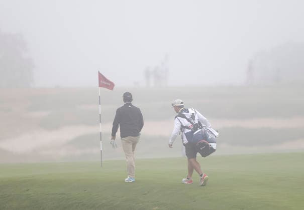 Alejandro Tosti of Argentina walks with his caddie as thick fog causes a delay in play during the first round of the 126th U.S. Open Golf Championship at Shinnecock Hills Golf Club in Southampton, NY, on Thursday, June 18, 2026.  NYC20260618802 JOHNxANGELILLO
