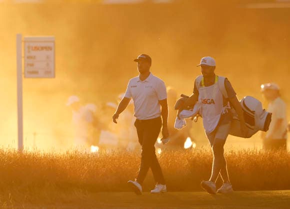 Wyndham Clark and caddie David Pelekoudas walk from the 18th tee box through rising dust from dry course conditions before sunset in the third round of the 126th U.S. Open Golf Championship at Shinnecock Hills Golf Club in Southampton, NY on Saturday, June 20, 2026.  NYC202606202025 JOHNxANGELILLO