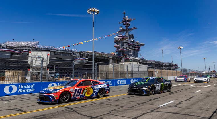SAN DIEGO, CA - JUNE 21: Chase Briscoe of the 19 Joe Gibbs Racing Bass Pro Shops Toyota and Ty Gibbs of the 54 Joe Gibbs Racing Monster Energy Toyota among the field passing turn 2 and the USS Carl Vinson (CVN70) during the Anduril 250 NASCAR, Motorsport, USA Cup Series Race, Sunday, June 21, 2026, at Naval Base Coronado in San Diego, California. (Photo by Tony Ding Icon Sportswire) AUTO: JUN 21 NASCAR Cup Series Anduril 250 Race the Base EDITORIAL USE ONLY Icon46520260621015250
