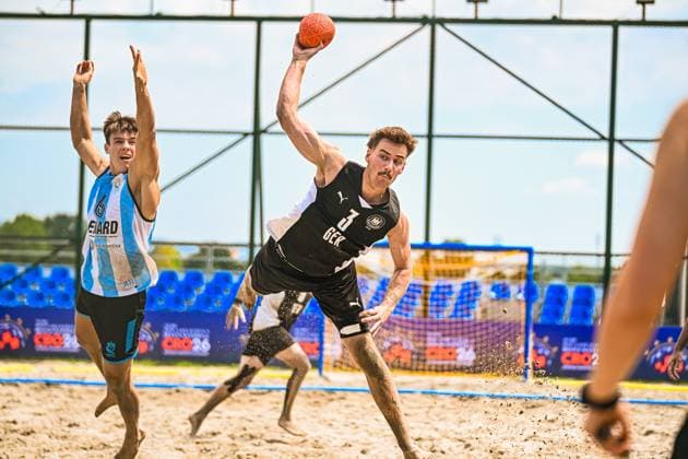 LIEBECK Lennart ( 3; Deutschland Beachhandball Nationalmannschaft) streckt sich im Sprung zum Wurf, Sand spritzt unter seinen Füßen auf. Ein argentinischer Gegenspieler ( 6) reißt die Arme hoch und versucht den Wurf zu blocken. IHF Beach Handball World Championship, WM, Weltmeisterschaft 2026, 23.06.2026, Zagreb, Jarun See *** LIEBECK, Lennart 3, Germany Copyright: xspeedshotx xDorianfrickx