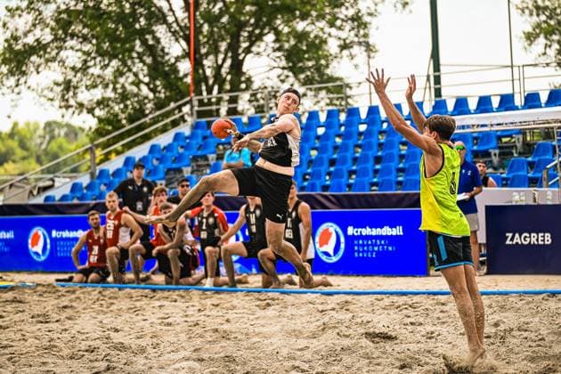 Ein Spieler der deutschen Beachhandball-Nationalmannschaft springt zum Wurf und wird von einem Gegner in Neongelb geblockt. Die Szene findet am Jarun See in Zagreb vor blauer Tribünenkulisse mit dem Schriftzug Zagreb statt. IHF Beach Handball World Championship, WM, Weltmeisterschaft 2026, 23.06.2026, Zagreb, Jarun See *** A player on the German national beach handball team jumps to take a shot and is blocked by an opponent wearing neon yellow. The scene takes place at Lake Jarun in Zagreb against the backdrop of blue bleachers bearing the inscription Zagreb IHF Beach Handball World Championship 2026, June 23, 2026, Zagreb, Lake Jarun,detected_source_language Copyright: xspeedshotx xDorianfrickx