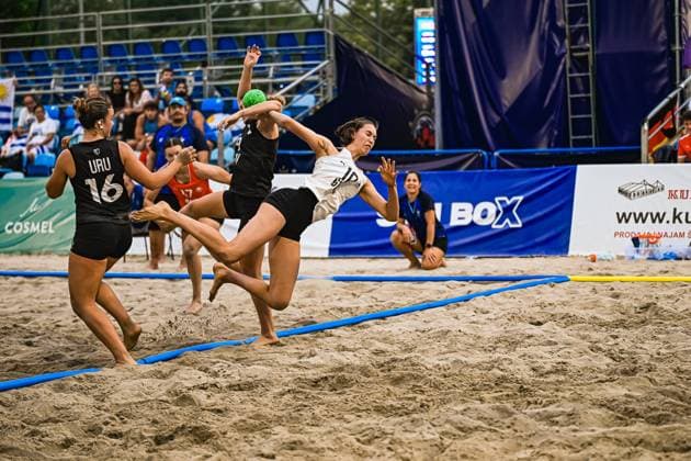 Eine Spielerin im weißen Trikot springt zum Wurf und wird dabei von zwei Gegenspielerinnen in schwarzen URU-Trikots bedrängt. Der grüne Ball ist klar im Bild sichtbar, die Szene zeigt maximale Körperspannung im Sand. IHF Beach Handball World Championship, WM, Weltmeisterschaft 2026, 23.06.2026, Zagreb, Jarun See *** A player in a white jersey jumps to take a shot while being pressured by two opponents in black URU jerseys. The green ball is clearly visible in the frame; the scene shows maximum body tension on the sand. IHF Beach Handball World Championship 2026, June 23, 2026, Zagreb, Lake Jarun,detected_source_language Copyright: xspeedshotx xDorianfrickx