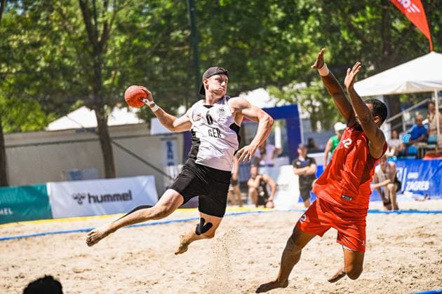 Lars Zelser ( 6; Deutschland Beachhandball Nationalmannschaft) springt mit dem Ball in der Hand zum Wurf ab, während ein Gegner in Rot die Arme hochreißt. Die Szene findet im Sand am Jarun See in Zagreb statt. IHF Beach Handball World Championship, WM, Weltmeisterschaft 2026, 23.06.2026, Zagreb, Jarun See *** Lars Zelser 6, a member of the German national beach handball team, jumps to shoot with the ball in his hand, while an opponent in red throws his arms up. The scene takes place on the sand at Lake Jarun in Zagreb. IHF Beach Handball World Championship 2026, June 23, 2026, Zagreb, Lake Jarun Copyright: xspeedshotx xDorianfrickx