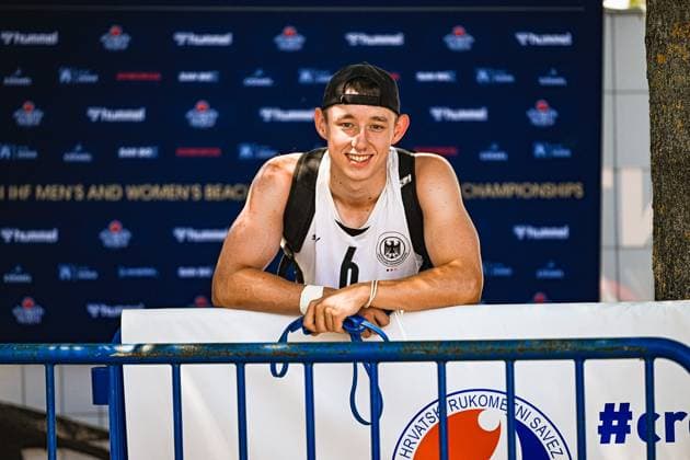 Lars Zelser ( 6; Deutschland Beachhandball Nationalmannschaft) lehnt lächelnd an einer blauen Absperrung vor dem offiziellen EHF-Backdrop der Beach-Handball-Europameisterschaft in Zagreb. Er trägt einen Rucksack und eine schwarz-weiße Kappe. IHF Beach Handball World Championship, WM, Weltmeisterschaft 2026, 23.06.2026, Zagreb, Jarun See *** Lars Zelser, a member of the German national beach handball team, leans smiling against a blue barrier in front of the official EHF backdrop at the Beach Handball European Championship in Zagreb. He is wearing a backpack and a black-and-white cap. IHF Beach Handball World Championship 2026, June 23, 2026, Zagreb, Lake Jarun Copyright: xspeedshotx xDorianfrickx