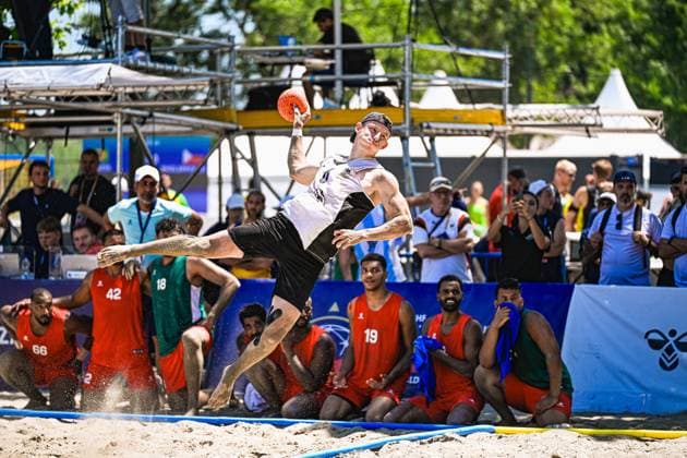 Ein Spieler der deutschen Beachhandball-Nationalmannschaft vollführt einen athletischen Sprungwurf mit dem Ball in der erhobenen Hand, Sand spritzt unter seinen Füßen auf. Im Hintergrund verfolgen Zuschauer und Spieler des Gegners das Spiel am Jarun See in Zagreb. IHF Beach Handball World Championship, WM, Weltmeisterschaft 2026, 23.06.2026, Zagreb, Jarun See *** A player on the German national beach handball team performs an athletic jump shot with the ball held aloft; sand sprays up beneath his feet. In the background, spectators and players from the opposing team watch the game at Lake Jarun in Zagreb during the 2026 IHF Beach Handball World Championship, June 23, 2026, Zagreb, Lake Jarun Copyright: xspeedshotx xDorianfrickx