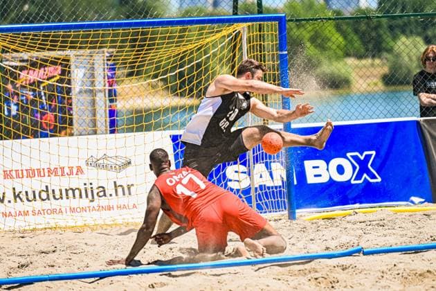 Ein Spieler der Deutschen Beachhandball Nationalmannschaft springt dynamisch am Tor und versucht den Ball zu verwerten, während ein Gegenspieler in rotem Trikot ( 17) im Sand liegt. Sand spritzt auf, der Ball ist direkt vor dem Tor sichtbar. IHF Beach Handball World Championship, WM, Weltmeisterschaft 2026, 23.06.2026, Zagreb, Jarun See *** A player on the German national beach handball team leaps dynamically toward the goal and attempts to score, while an opponent in a red jersey with the number 17 lies in the sand. Sand flies up; the ball is visible directly in front of the goal. 2026 IHF Beach Handball World Championship, June 23, 2026, Zagreb, Lake Jarun Copyright: xspeedshotx xDorianfrickx