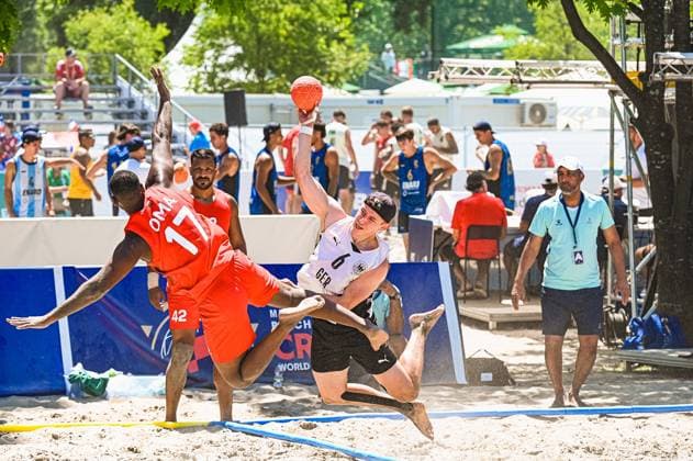 Lars Zelser ( 6; Deutsche Beachhandball Nationalmannschaft) springt mit dem Ball in der Hand hoch und trifft auf einen Gegenspieler Omans ( 17) im Zweikampf am Jarun See in Zagreb. Sand spritzt auf, während beide Spieler in der Luft kollidieren. IHF Beach Handball World Championship, WM, Weltmeisterschaft 2026, 23.06.2026, Zagreb, Jarun See *** Lars Zelser, No. 6 on the German national beach handball team, jumps with the ball in his hand and collides with an Omani opponent, No. 17, during a one-on-one battle at Lake Jarun in Zagreb. Sand flies up as both players collide in midair. 2026 IHF Beach Handball World Championship, June 23, 2026, Zagreb, Lake Jarun Copyright: xspeedshotx xDorianfrickx