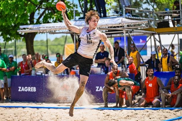 Tim KRAUTH ( 17; Deutschland Beachhandball Nationalmannschaft) springt mit dem Ball in der erhobenen Hand zum Wurf ab und wirbelt Sand auf. Im Hintergrund sind Gegenspieler in roten Trikots sowie Zuschauer am Jarun See in Zagreb zu sehen. IHF Beach Handball World Championship, WM, Weltmeisterschaft 2026, 23.06.2026, Zagreb, Jarun See *** Tim KRAUTH 17, a member of the German national beach handball team, jumps to shoot with the ball held aloft, kicking up sand. In the background, opponents in red jerseys and spectators can be seen at Lake Jarun in Zagreb. 2026 IHF Beach Handball World Championship, June 23, 2026, Zagreb, Lake Jarun Copyright: xspeedshotx xDorianfrickx
