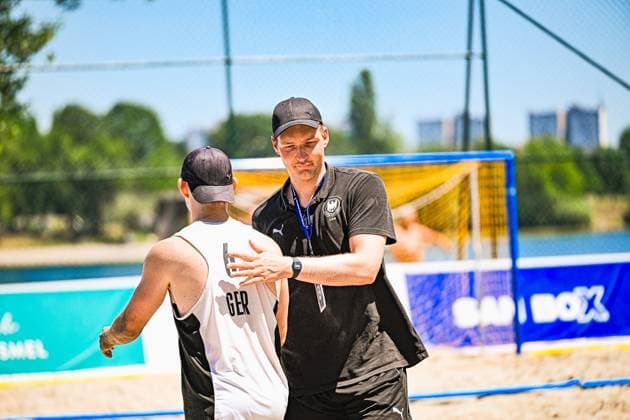 Ein Trainer im schwarzen DHB-Shirt gibt einem Spieler der deutschen Beachhandball-Nationalmannschaft taktische Anweisungen am Sandplatz in Zagreb. Im Hintergrund ist das Beachhandball-Tor am Jarun See zu sehen. IHF Beach Handball World Championship, WM, Weltmeisterschaft 2026, 23.06.2026, Zagreb, Jarun See *** A coach in a black DHB shirt gives tactical instructions to a player on the German national beach handball team on the sand court in Zagreb. The beach handball goal at Lake Jarun can be seen in the background. IHF Beach Handball World Championship 2026, June 23, 2026, Zagreb, Lake Jarun Copyright: xspeedshotx xDorianfrickx
