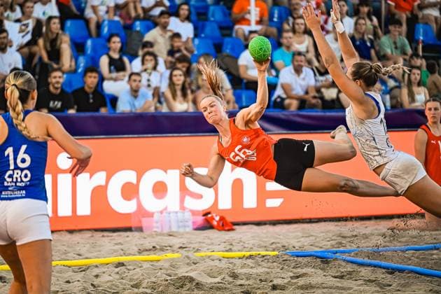 Eine Spielerin im orangefarbenen Torwarttrikot wirft aus der Luft auf das Tor, während eine Gegenspielerin den Block versucht. Im Vordergrund ist eine kroatische Spielerin ( 16, CRO) zu sehen. IHF Beach Handball World Championship, WM, Weltmeisterschaft 2026, 23.06.2026, Zagreb, Jarun See *** A player in an orange goalkeeper jersey shoots at the goal while in mid-air, as an opposing player attempts to block the shot. In the foreground is a Croatian player, No. 16, CRO. IHF Beach Handball World Championship 2026, June 23, 2026, Zagreb, Lake Jarun Copyright: xspeedshotx xDorianfrickx