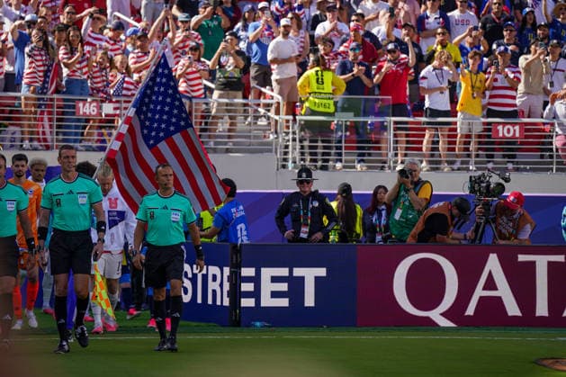 USA: Fußball FIFA World Cup, WM, Weltmeisterschaft, Fussball 2026, Sechzehntelfinale - USA vs Bosnien - Herzegowina im Levi™s Stadium (Santa Clara, San Francisco Bay Area, Kalifornien): Schiedsrichterteam führt die Mannschaften vor dem Spiel der FIFA Fußball-Weltmeisterschaft 2026 mit einer großen US-Flagge ins Levi™s Stadium. Im Hintergrund jubelnde US-Fans auf der Tribüne. Am Spielfeldrand Polizei, Fotografen, TV-Kamerateam und Volunteers. Werbebande mit Qatar Airways. Einlaufzeremonie, Fahne, Zuschauer, Fankultur, Sicherheit, Medien, Sportstätte, Innenansicht. *** USA Soccer 2026 FIFA World Cup, Round of 32: USA vs. Bosnia and Herzegovina at Levi’s Stadium in Santa Clara, San Francisco Bay Area, California. The referee team leads the teams onto the field before the 2026 FIFA World Cup match, carrying a large U.S. flag into Levi’s™s Stadium. In the background, cheering U.S. fans in the stands. On the sidelines: police, photographers, a TV camera crew, and volunteers. A Qatar Airways advertising banner. Parade of nations, flag, spectators, fan culture, security, media, sports venue, interior view Copyright: xJOERANxSTEINSIEKx