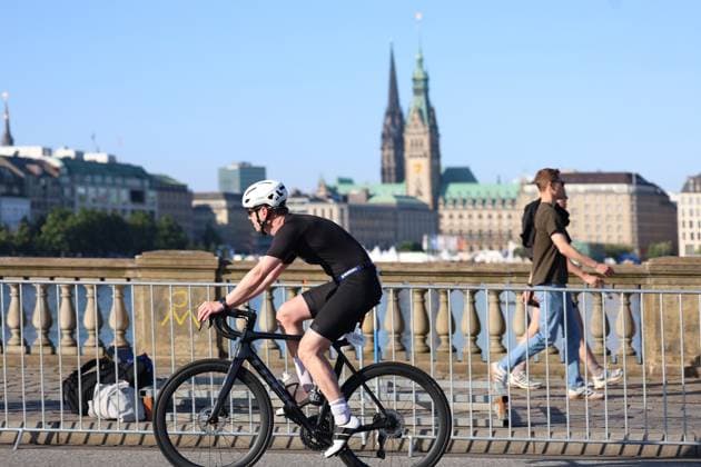 Ein Triathlet in schwarzem Einteiler fährt auf einem schwarzen Rennrad an der Binnenalster entlang, im Hintergrund ist das Hamburger Rathaus zu sehen. Die Startnummer 1006 ist am Rad befestigt. Triathlet ( 1006) auf der Radstrecke am Jungfernstieg Hamburg *** A triathlete in a black one-piece suit rides a black road bike along the Binnenalster; Hamburg City Hall can be seen in the background. Bib number 1006 is attached to the bike. Triathlete 1006 on the bike course at Jungfernstieg, Hamburg Copyright: xspeedshotx xSarahxWolfx