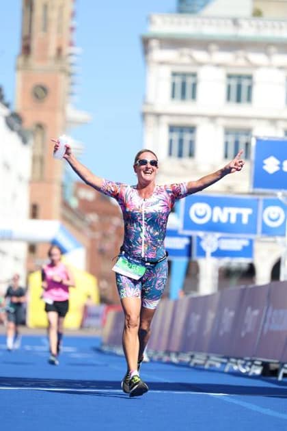 Eine Athletin überquert jubelnd die Ziellinie beim Triathlon am Jungfernstieg in Hamburg. Sie trägt ein farbenfrohes Wettkampf-Outfit in Pink und Blau mit Blumenmuster, Sonnenbrille und grüner Schwimmkappe. Im Hintergrund sind historische Hamburger Gebäude und die blaue Veranstaltungsinfrastruktur sichtbar, Mateo Ariza ( 13283, Kurzdistanz) Triathletin im Zieleinlauf am Jungfernstieg Hamburg, Mateo Ariza 13283 *** An athlete crosses the finish line jubilantly at the triathlon on Jungfernstieg in Hamburg. She is wearing a colorful competition outfit in pink and blue with a floral pattern, sunglasses, and a green swim cap. In the background, historic Hamburg buildings and the blue event infrastructure are visible, Mateo Ariza 13283, short-distance triathlete crossing the finish line at Jungfernstieg in Hamburg, Mateo Ariza 13283 Copyright: xspeedshotx xSarahxWolfx