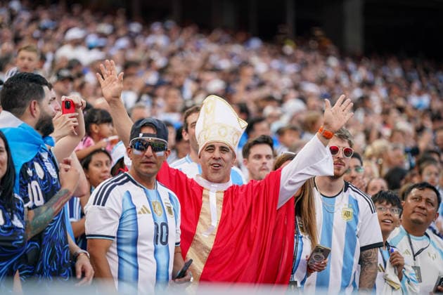 USA: Fussball FIFA World Cup, WM, Weltmeisterschaft, Fussball 2026, Viertelfinale - Argentinien vs Schweiz - Kansas City Stadium (GEHA Field at Arrowhead Stadium, Kansas City, Missouri): Argentinischer Fußballfan in einem als Papst gestalteten Kostüm feiert gemeinsam mit Anhängern der Albiceleste auf der Tribüne beim Viertelfinale der FIFA Fußball-Weltmeisterschaft 2026. Fans tragen Trikots und Fanaccessoires in den Nationalfarben und sorgen für ausgelassene Stimmung. Fankultur, Zuschauer, Tribüne, Fanblock, Argentinien, Albiceleste, Fankostüm, Papstkostüm, Porträt, Fußball, WM 2026. *** USA Soccer 2026 FIFA World Cup, Quarterfinal: Argentina vs. Switzerland, Kansas City Stadium (GEHA Field at Arrowhead Stadium), Kansas City, Missouri An Argentine soccer fan dressed in a Pope costume celebrates alongside Albiceleste supporters in the stands during the quarterfinals of the 2026 FIFA World Cup. Fans wear jerseys and fan gear in the national colors, creating a lively atmosphere. Fan culture, spectators, stands, fan section, Argentina, Albiceleste, fan costume, Pope costume, portrait, soccer, 2026 World Cup Copyright: xJOERANxSTEINSIEKx
