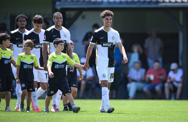 Fussball 1. Bundesliga 2026 2027 Testspiel 11.07.2026 SV Elversberg - FC Thun Noah Darvich, Jan Gyamerah, Frederik Schmahl und Filimon Gerezgiher (v.re, alle SV Elversberg) kommen mit Einlaufkinder auf das Spielfeld *** Soccer, Bundesliga 1, 2026–2027, Friendly Match, July 11, 2026, SV Elversberg vs. FC Thun: Noah Darvich, Jan Gyamerah, Frederik Schmahl, and Filimon Gerezgiher (from left to right), all from SV Elversberg, enter the field with the ball girls.