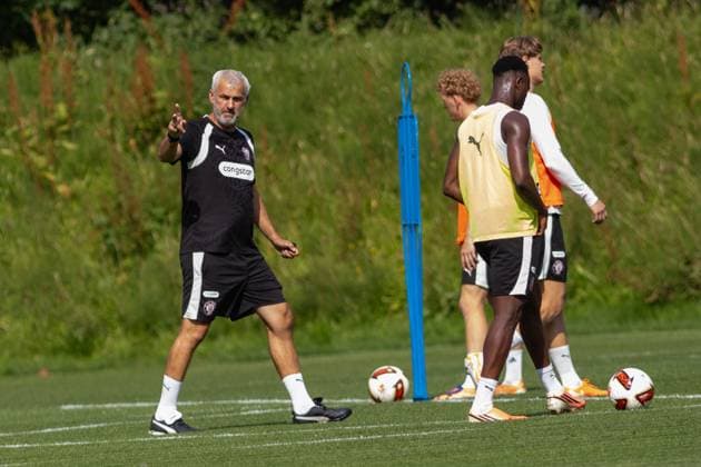 Ein Trainer des FC St. Pauli gibt auf dem Trainingsplatz mit ausgestrecktem Arm Anweisungen an seine Spieler. Mehrere Spieler in gelben und orangefarbenen Leibchen hören zu, auf dem Rasen liegen Fußbälle. Trainer gibt Anweisungen beim FC St. Pauli Training in Hamburg *** An FC St. Pauli coach stands on the practice field with his arm outstretched, giving instructions to his players. Several players in yellow and orange vests are listening; soccer balls lie on the grass. The coach gives instructions during an FC St. Pauli practice in Hamburg. Copyright: xAndreasxTolksdorfx