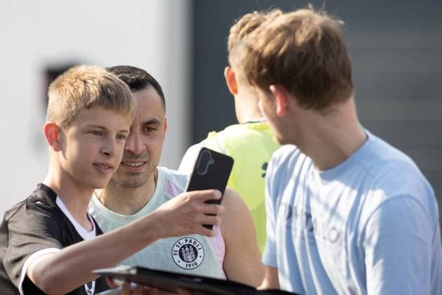Ein FC St. Pauli Spieler macht gemeinsam mit zwei jungen Fans ein Selfie mit dem Smartphone am Trainingszentrum in Hamburg. Ein weiterer Fan steht rechts im Bild. Manos Saliakas ( 2 FC St. Pauli) beim Selfie mit Fans am Trainingszentrum *** An FC St. Pauli player takes a selfie with two young fans using a smartphone at the training center in Hamburg. Another fan is standing on the right side of the picture. Manos Saliakas of FC St. Pauli takes a selfie with fans at the training center. Copyright: xAndreasxTolksdorfx