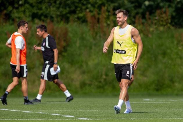 Ein Spieler des FC St. Pauli mit der Rückennummer 21 läuft lächelnd über den Trainingsplatz, im Hintergrund sind ein weiterer Spieler und ein Betreuer mit Unterlagen zu sehen. Das Training findet bei sonnigem Wetter im Trainingszentrum in Hamburg statt. Lars Ritzka 21 beim Training im Trainingszentrum Hamburg *** An FC St. Pauli player wearing jersey number 21 runs across the practice field with a smile; in the background, another player and a coach can be seen holding documents. The practice is taking place in sunny weather at the training center in Hamburg. Lars Ritzka (21) during practice at the Hamburg training center Copyright: xAndreasxTolksdorfx